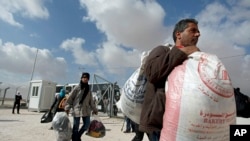 Newly-arrived Syrian refugees carry their belongings upon their arrival to the new Jordanian-Emirati refugee camp, Mrajeeb al-Fhood, in Zarqa, Jordan, April 10, 2013. 