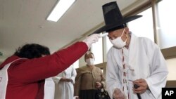 A S. Korean Confucian scholar wearing a face mask to help protect against the spread of the new coronavirus has his temperature checked upon his arrival to cast his vote for parliamentary elections at a polling station in Nonsan, S. Korea, April 15, 2020.