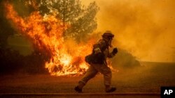 A firefighter runs while trying to save a home as a wildfire tears through Lakeport, Calif., Tuesday, July 31, 2018.