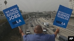 South Los Angeles resident Christian Del Cid waves banners calling for good jobs, on a bridge in front of oncoming traffic at the Interstate I-110 overpass on a "structurally deficient" bridge to call on U.S. Congress to provide funding for highway improv