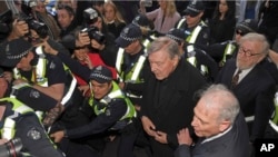 Kardinal George Pell (tengah kanan) dikawal oleh polisi saat tiba di Pengadilan Melbourne. Australia, 26 Juli 2017. 