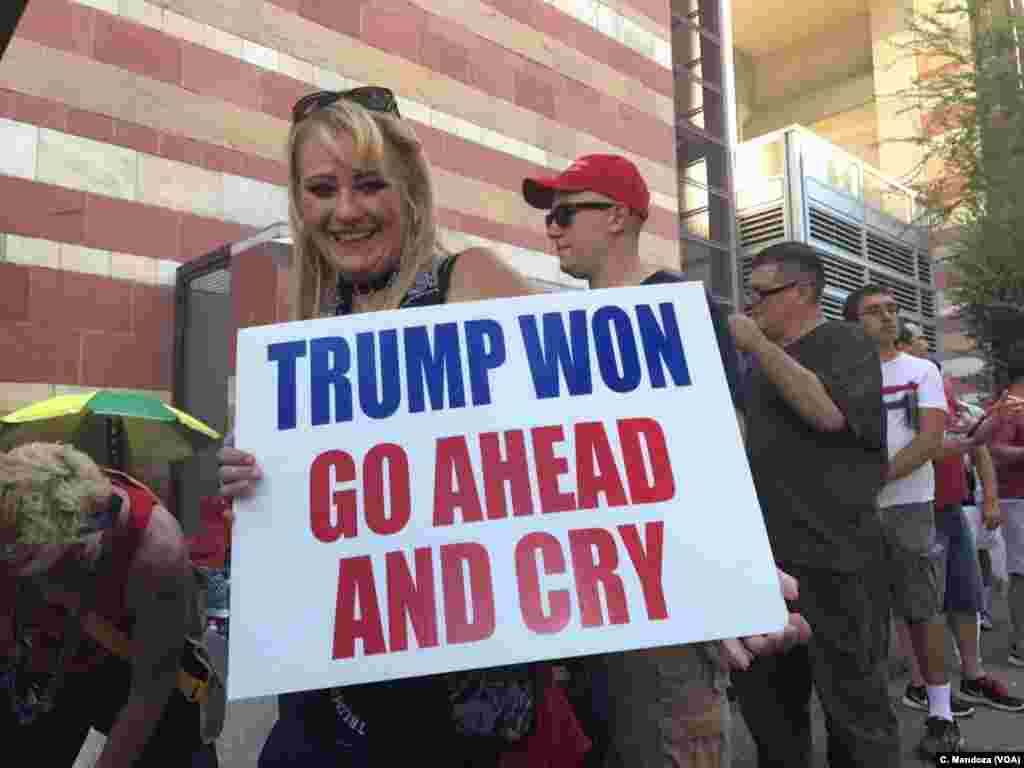 A woman waiting in line to get into the convention center, where President Donald Trump was scheduled to hold a campaign-style rally, holds a sign, in Phoenix, Aug. 22, 2017. 
