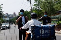 Security personnel and a delivery worker are seen at an entrance to a residential area under lockdown near the Xinfadi wholesale market, following cases of the coronavirus disease (COVID-19) infections, in Beijing, June 16, 2020.