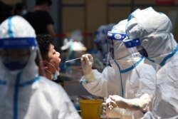 FILE - Medical workers in protective suits collect a swab from a resident for nucleic acid testing at a sports center in Jiangning district, following new cases of the coronavirus, in Nanjing, Jiangsu province, China, July 21, 2021.
