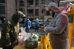 A resident collects vegetables purchased through group orders at the entrance of a residential compound in Wuhan, the epicenter of the coronavirus outbreak, in Hubei province, China, Feb. 21, 2020.