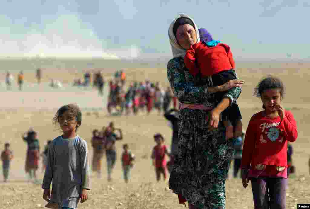Displaced people from the minority Yazidi sect, fleeing violence from forces loyal to the Islamic State in Sinjar town, walk toward the Syrian border on the outskirts of Sinjar mountain near the Syrian border town of Elierbeh of Al-Hasakah Governorate, Aug. 11, 2014.