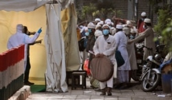 FILE - Indian paramedics, left, screen Muslims to be taken by bus to a coronavirus quarantine facility, in the Nizamuddin area of New Delhi, India, March 31, 2020.