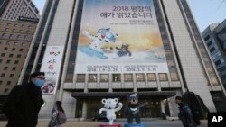 People pass a banner promoting the upcoming 2018 Pyeongchang Winter Olympic as official mascots, a white tiger 'Soohorang' for the Olympic, and the Asiatic black bear "Bandabi" for the Paralympic (Bottom-R) are displayed in downtown in Seoul, South Korea, Jan. 9, 2018.