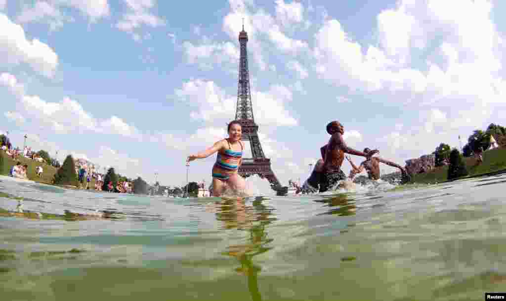 Anak-anak remaja mendinginkan diri di air mancur di Lapangan Trocadero di depan Menara Eiffel pada siang hari yang panas di Paris.