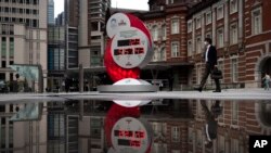 A countdown clock for the Tokyo 2020 Olympics is reflected in a puddle of water outside Tokyo Station in Tokyo, March 23, 2020. 