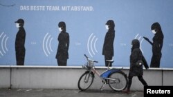 Seorang perempuan berjalan melewati poster bertuliskan "Tim terbaik. Dengan (menjaga) jarak." di depan pabrik BMW, di tengah naiknya kasus Covid-19 di Munich, Jerman, 9 Desember 2020. (REUTERS/Andreas Gebert)