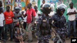 Ugandan riot police stand close to dejected opposition supporters to prevent them from demonstrating, shortly after the election result was announced, in downtown Kampala, Uganda, Feb. 20, 2016. 