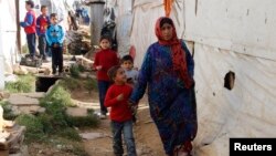 FILE - Syrian refugees walk in an informal settlement in Zahle in the Bekaa Valley, Lebanon, Oct. 16, 2014. 