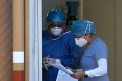 FILE - Medical workers look over paperwork at the entrance to the COVID-19 triage area at the Mexico General Hospital, in Mexico City, May 12, 2020.
