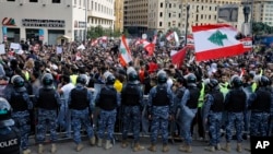 Anti-government protesters hold Lebanese flags and chant slogans as riot police stand guard in front of the government building, in central Beirut, Lebanon, Dec. 23, 2018.