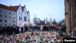 Warga mengamati bunga dan lilin yang ditinggalkan untuk menghormati para korban di dekat pasar Natal 'Alter Markt', tempat seorang pria menabrakkan mobil ke kerumunan melalui rute keluar darurat pada Jumat malam, di Magdeburg, Jerman, 22 Desember 2024. (Annegret Hilse/REUTERS)