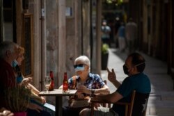 A woman, partially wearing a face mask, sits in a terrace bar in Barcelona, Spain, July 9, 2020.
