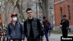 FILE - A student wearing a mask to protect against the coronavirus walks with others at Harvard University, before the school moved its classes to online-only, in Cambridge, Massachusetts, March 10, 2020.