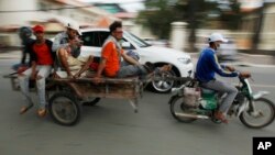A Cambodian worker, third from left, views his mobile phone on a motor cart forwarding to work, in Phnom Penh, Cambodia, Tuesday, Aug. 11, 2015. Mobile phones are more popular than desktop computers in Cambodia. (AP Photo/Heng Sinith)