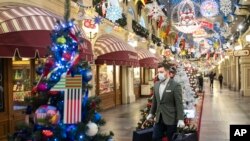 Seorang pria mengenakan masker dan sarung tangan, membawa barang-barang belanjaannya di antara toko-toko di Departemen Luar Negeri GUM di Moskow, Rusia, yang berhiaskan dekorasi Natal dan Tahun Baru, 23 November 2020. 