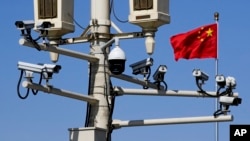 Bendera nasional Tiongkok berkibar di dekat kamera pengintai yang dipasang di tiang lampu di Lapangan Tiananmen di Beijing, 15 Maret 2019. (Foto: AP)