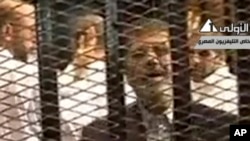FILE - Video broadcast on Egyptian State Television shows ousted President Mohammed Morsi speaking from inside a mesh cage as he stands with other defendants during a court hearing at a police academy compound in Cairo, Egypt.