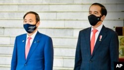 In this photo released by Indonesian Presidential Palace, Japanese Prime Minister Yoshihide Suga, left, and Indonesian President Joko Widodo listen to the national anthems during their meeting at the Presidential Palace in Bogor West Java, Oct 20, 2020..