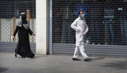 A man wearing a face mask to protect against coronavirus and a woman, walk past shuttered shops on a usually bustling high street as the country continues its lockdown to help curb the spread of the virus, in London, April 27, 2020.