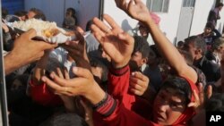 FILE - Displaced Iraqis from the Yazidi community gather for food at the Nowruz camp, in Derike, Syria, Aug. 12, 2014. 