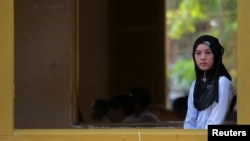 A Muslim invigilator stands near a window as students sit for their final examinations at the Sisowath High School in central Phnom Penh, Cambodia, August 22, 2016.