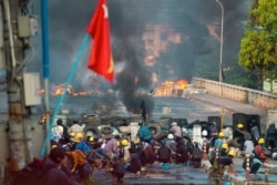 Anti-coup protesters take cover at a barricade as they clash with security forces on Bayint Naung Bridge in Mayangone, Yangon, Myanmar, March 16, 2021.