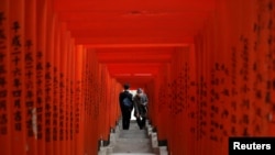 Pengunjung yang mengenakan masker pelindung wajah berjalan melalui gerbang torii kayu berwarna merah di sebuah kuil, di tengah wabah Covid-19, di Tokyo, Jepang, 22 Desember 2020. (Foto: Reuters)
