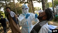 FILE - A medical official wearing a Personal Protective equipment suit takes a swab sample from a members of the Loya jirga (grand assembly of Afghan elders) to test for the COVID-19 coronavirus in Kabul, Aug. 5, 2020. 