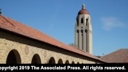 FILE- People walk on the Stanford University campus beneath Hoover Tower in Stanford, Calif., March 14, 2019. 