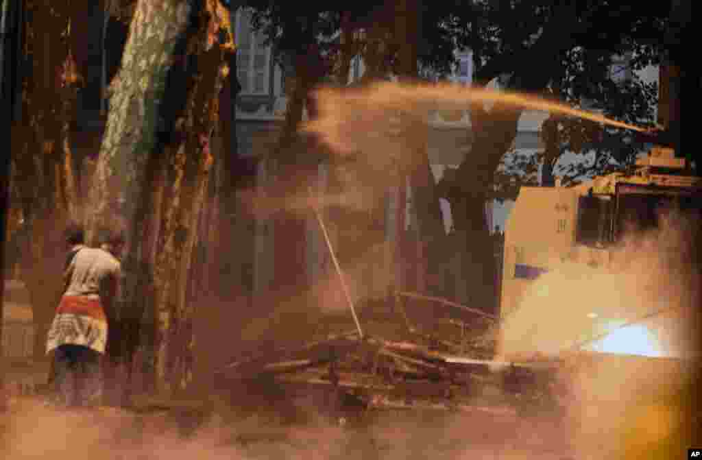 Polisi menggunakan meriam air saat para demonstran bersembunyi di belakang pohon dalam protes anti-pemerintah di Besiktas, Istanbul (2/6). (AP/Thanassis Stavrakis)