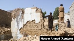 Warga berdiri di tengah puing-puing rumah yang rusak akibat gempa di Harnai, Balochistan, Pakistan, 7 Oktober 2021. (Foto: REUTERS/Naseer Ahmed)