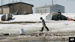 FILE - A young boy walks along the frozen banks of the Newtok River, in Newtok, Alaska, Wednesday, May 24, 2006, past frozen human waste dumped because the village lacks indoor plumbing.