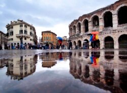 FILE - Tourists walk in the pouring rain along the old arena, right, and buildings of the old town in Verona, Italy, April 23, 2019.