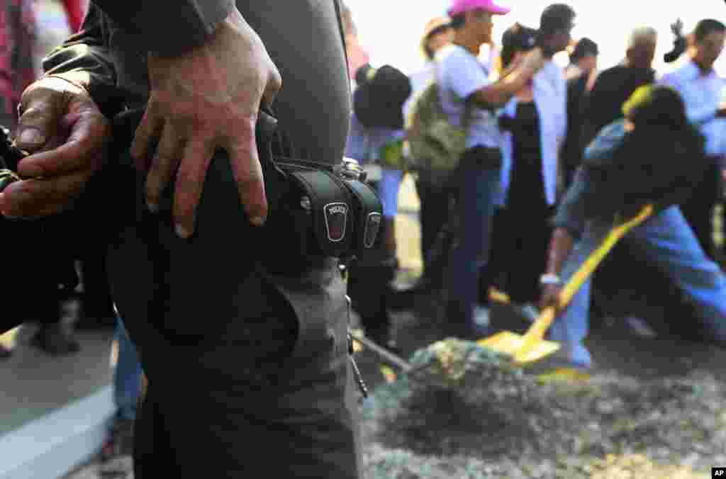 A police officer watches pro-government supporters building a barricade to block the gate of National Anti-Corruption Commission office in Bangkok, Feb. 27, 2014.