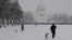Orang-orang berjalan-jalan dengan anjingnya di sepanjang National Mall saat salju turun selama badai musim dingin di Washington, DC pada 6 Januari 2025. (Foto: AFP)