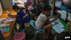 Coleen Giselle Ahilon (kiri) dan Churt Iverson Steven Ordones (kanan) memulai sekolah dari rumah dengan menggunakan ponsel dan modul pembelajaran yang sudah dicetak, di pinggiran kota kota Mandaluyong, Manila, 5 Oktober 2020. (Foto: Maria Tan / AFP)