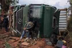 FILE - A passer-by looks inside an overturned truck in the middle of National Road 27 in Ituri Province, northeastern Democratic Republic of Congo, Sept. 16, 2020.