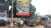 People pass in front of an electoral campaign poster for incumbent President Alpha Conde in Conakry, Guinea, Sept. 10, 2015. 