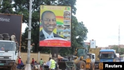 FILE - People pass in front of an electoral campaign poster for incumbent President Alpha Conde in Conakry, Guinea, Sept. 10, 2015. 