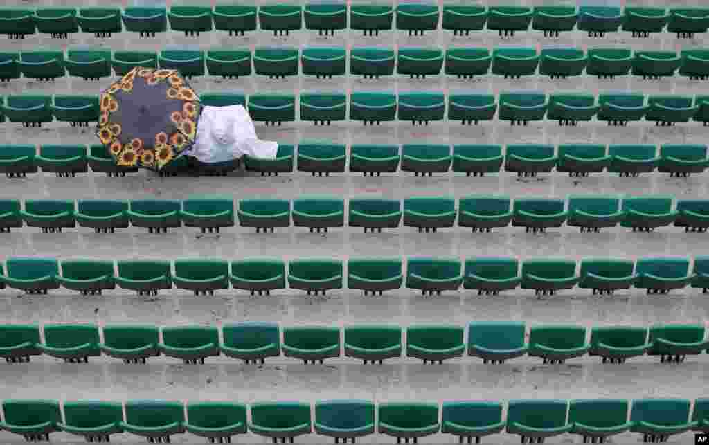 Seorang penonton duduk di bawah payung di stadion Roland Garros sementara pertandingan turnamen tenis Perancis Terbuka tertunda karena hujan di Paris.