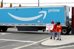 FILE - People hold a banner at the Amazon facility as members of a congressional delegation arrive to show their support for workers who will vote on whether to unionize, in Bessemer, Alabama, March 5, 2021.