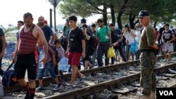 Des migrants marchent le long d'un chemin de fer.