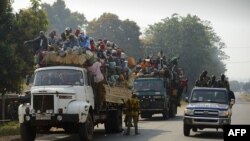 A national police car passes by Muslim Centrafricans riding aboard trucks on their way to their villages in Bangui, three days before elections for the next interim President of Centrafrica, Jan. 17, 2014.