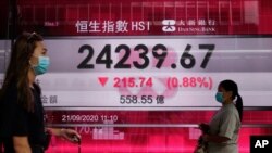 People wearing face masks walk past a bank's electronic board showing the Hong Kong share index at Hong Kong Stock Exchange Sept. 21, 2020. 