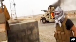 A militant standing in front of a burning Iraqi Army Humvee in Tikrit, Iraq, June 12, 2014. 